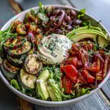 A close-up of a Vegan Mediterranean Buddha Bowl with creamy hummus, olives, and a drizzle of tahini dressing.
