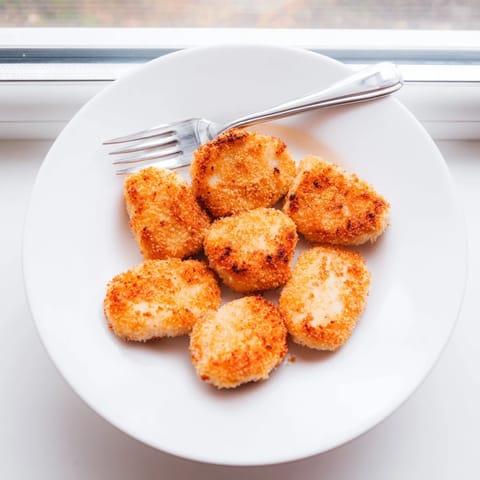 Freshly fried chicken nuggets arranged on a plate with dipping sauces and a side of french fries.