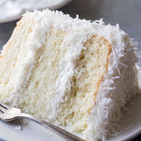 Freshly sliced wedges of Coconut Cake reveal tender crumb and creamy coconut filling, served on dessert plates next to steaming black tea.