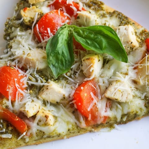 Close-up of a slice of Chicken Pesto Pizza, showcasing tender chicken, fragrant basil pesto, and bubbling cheese.  