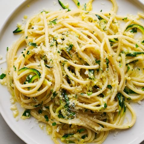 A vibrant plate of Lemon Zucchini Pasta features golden noodles, bright citrus zest, and a sprinkle of grated cheese.