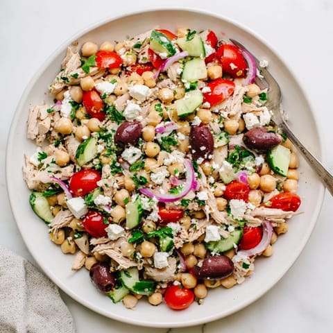 Vibrant Mediterranean Chickpea Chicken Salad in a white bowl, featuring halved cherry tomatoes, briny Kalamata olives, and fresh parsley garnish.  