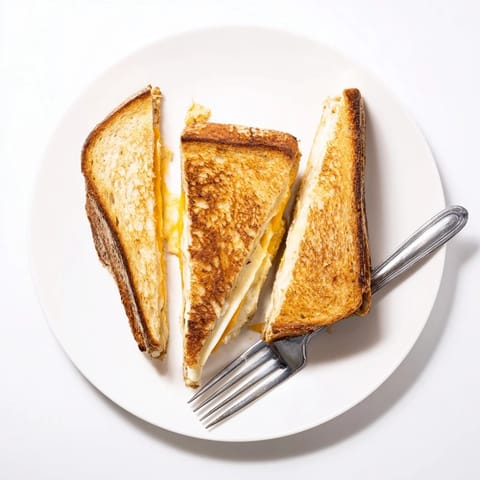A Triple Cheese Sourdough Grilled Cheese rests on a white plate beside a red bowl of creamy tomato soup for a cozy dinner.
