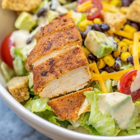 A close-up of Crunchy Taco Chicken Salad with seasoned chicken, black beans, corn, and crushed shells on romaine.