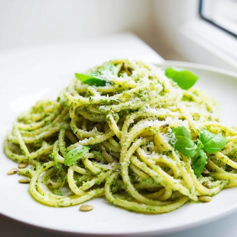 Steaming bowl of sunflower seed pesto pasta tossed in a vibrant green sauce, garnished with basil leaves and lemon zest.