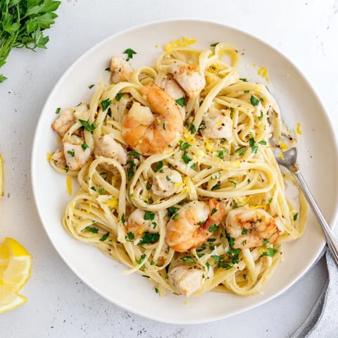 A close-up of tender shrimp and chicken nestled in pasta, garnished with lemon wedges and a sprinkle of red pepper flakes.  