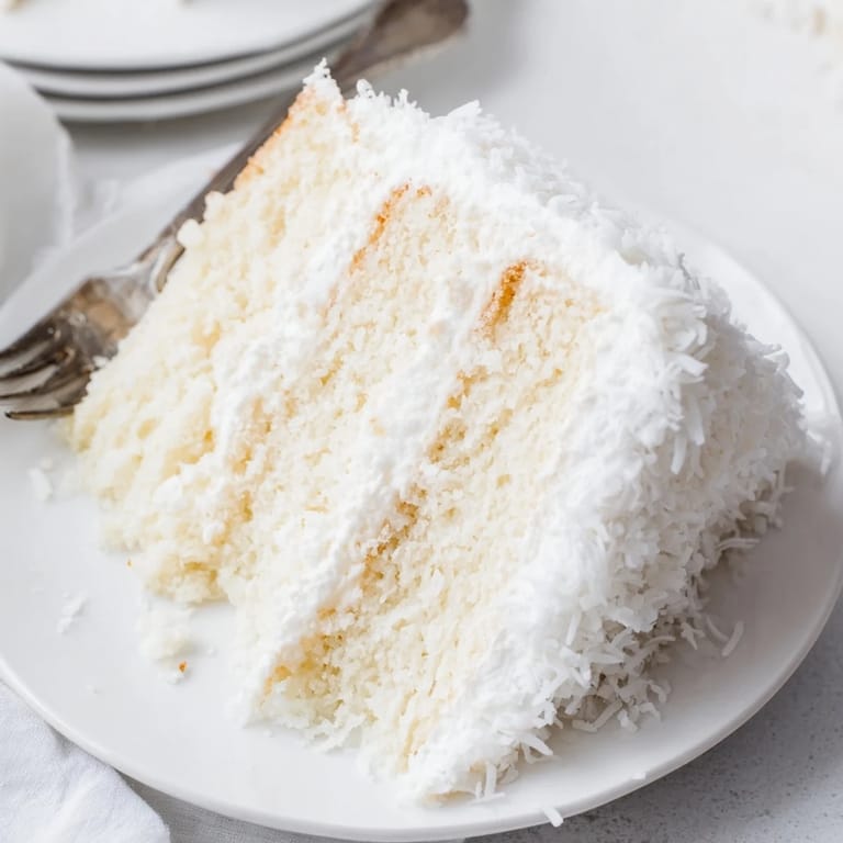 Classic layered Coconut Cake stands tall with snowy seven-minute frosting and shredded coconut, ready for a festive celebration or afternoon tea.