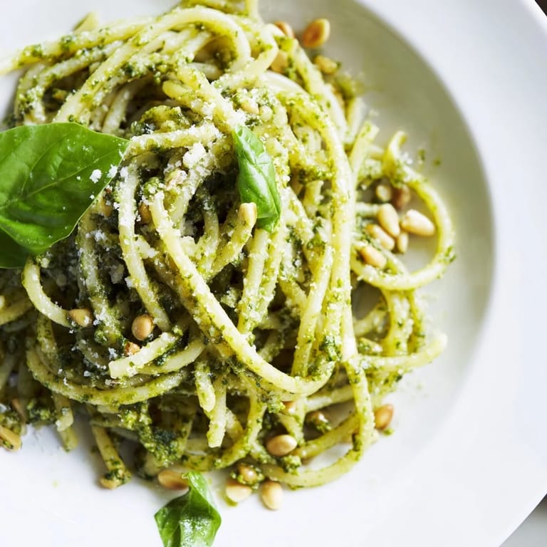 Sunflower seed pesto pasta served warm in a white bowl, drizzled with olive oil and accompanied by a glass of white wine.