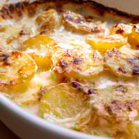 Golden-brown Au Gratin Potatoes bubbling with melted Gruyère and Parmesan in a ceramic baking dish, fresh from the oven.