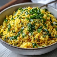 A vibrant bowl of Turmeric Cauliflower Rice, flecked with golden spices and fresh cilantro, served alongside grilled chicken.