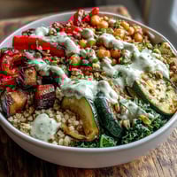 Freshly roasted eggplant and zucchini top a hearty bowl of Mediterranean Buddha Bowl meal prep, drizzled with creamy tahini dressing.