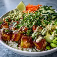 Golden-brown broiled salmon cubes rest on fluffy white rice with sliced cucumbers, carrots, and avocado, creating a vibrant Baked Salmon Rice Bowl.